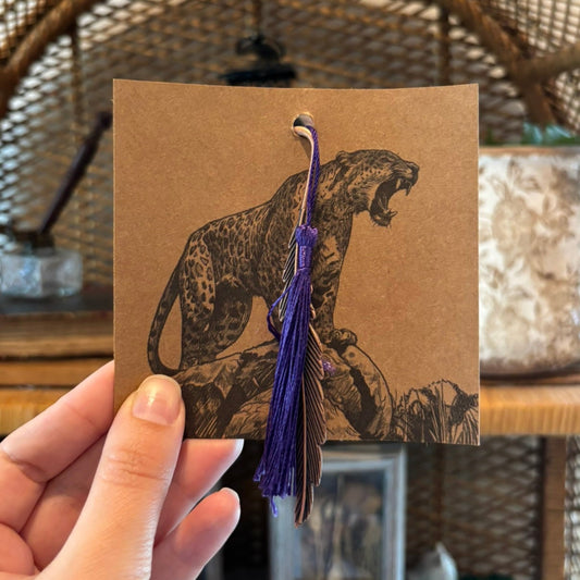Card with a leopard illustration and tassel held by a hand against a blurred background